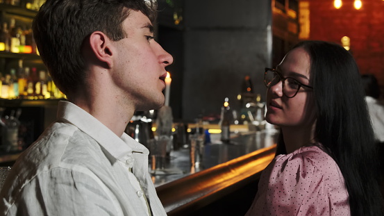 Pretty couple spend time in cozy pub with bar counter in blurred background. Serious man tells story to interested woman