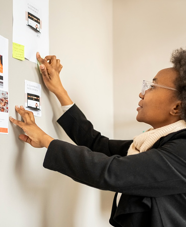 African businesswoman sticking her business advertising flyer on wall in creative office