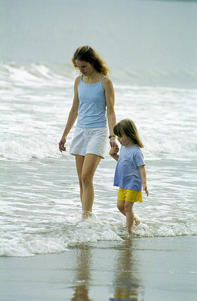 istock mother and daughter walking in surf on beach 173541150
