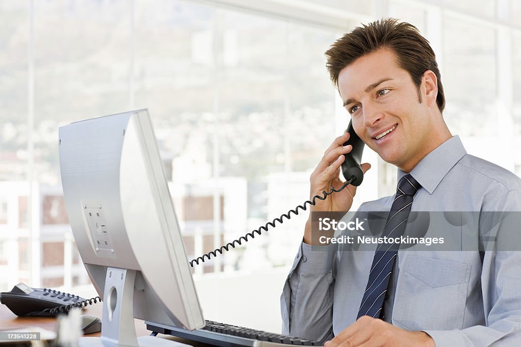 Homme d'affaires parler sur un téléphone assis par ordinateur - Photo de 20-24 ans libre de droits