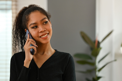 Happy smiling African black teenage woman with curly hair having a nice conversation on the phone.