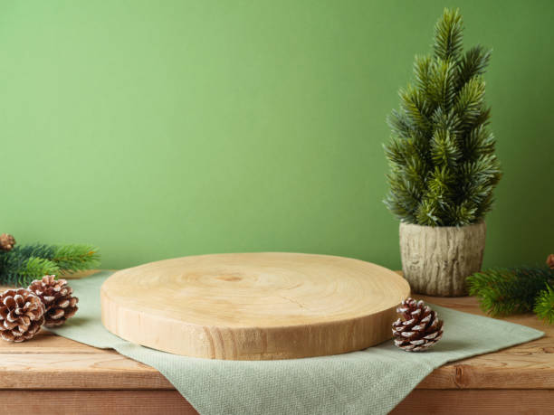 istock Empty log podium with tablecloth on wooden table over green wall and pine tree decoration background. Christmas mock up for design and product display. 1735430931