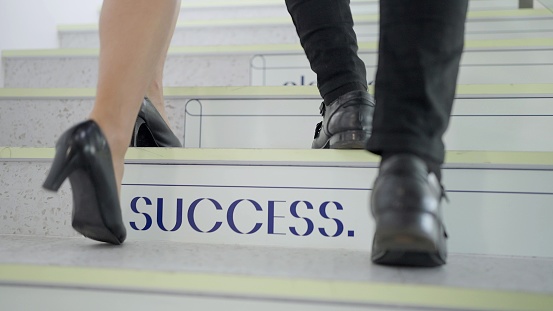 Close up stepping of businessman and woman walking up on the stairs at office. Two businesspeople going up the stairs together. Business growth up concept