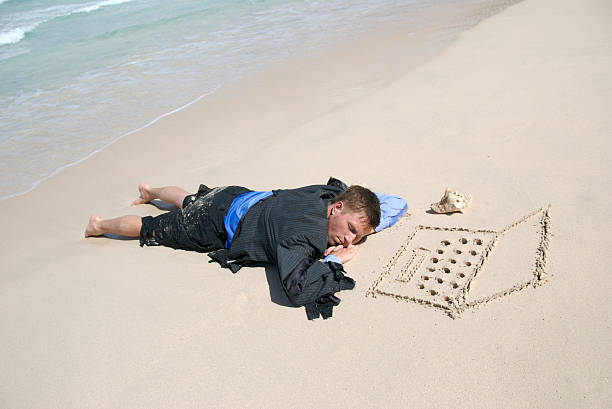 náufrago empresario durmiendo en su computadora portátil en la playa - stranded fotografías e imágenes de stock