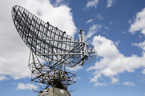 A radar dish in a blue sky with puffy white clouds. This was used for monitoring aircraft.