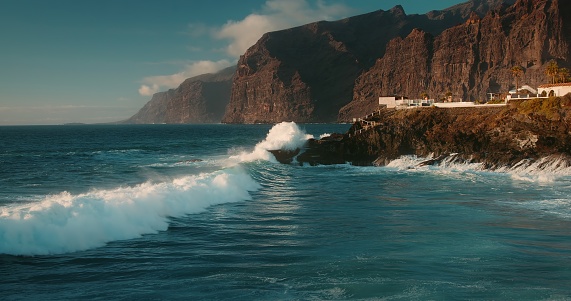 Big ocean waves crash on black volcanic rocks on shore of Tenerife Island. Cinematic view deep blue ocean swell violently splashing over the rocky coast of an exotic island.