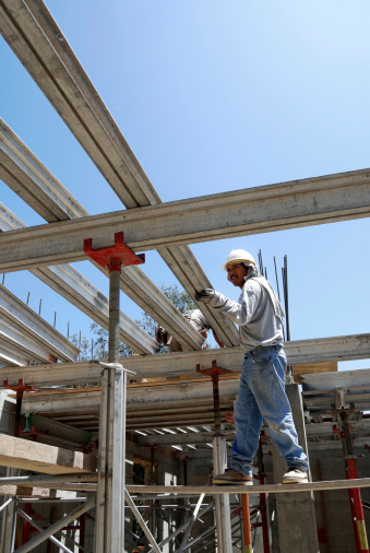 A worker slides a shoring beam into place while standing on scaffold.