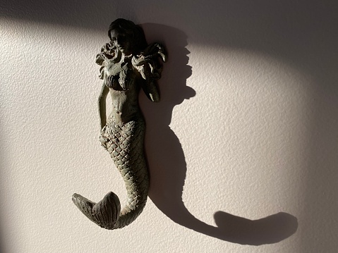 Mermaid mounted to a wall with a long shadow