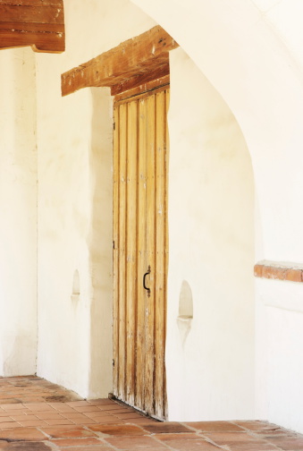 Mission church entrance door with wood timber surrounded by white stucco and clay tile floor.  Mission San Juan Capistrano, California, 2008.
