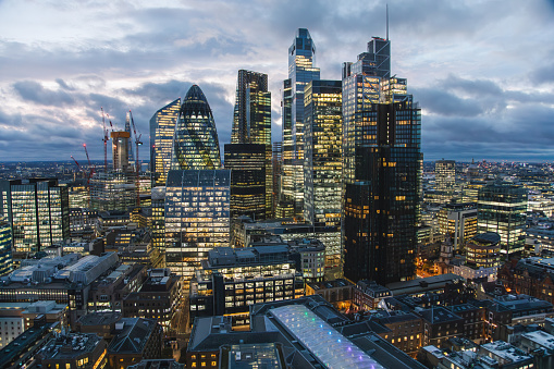 Aerial panoramic view of The City of London cityscape skyline with metropole financial district modern skyscrapers after sunset on night with illuminated buildings and cloudy sky in London, UK