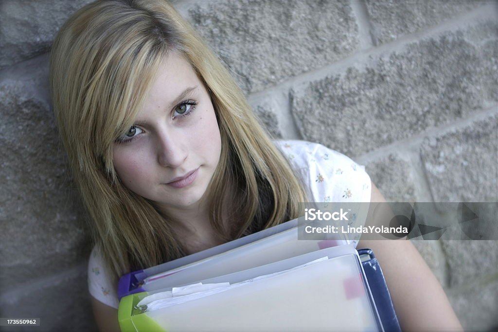 Teenage Student Young teen leaning against brick wall holding books and binders. Brick Wall Stock Photo