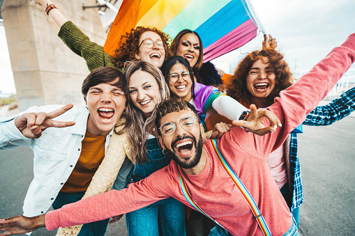 Diverse group of cheerful young people celebrating gay pride day - Lgbt community concept with guys and girls hugging together outdoors