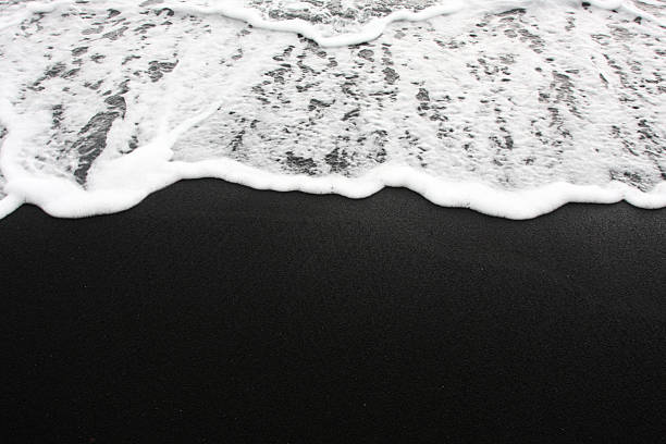 Black Sand Beach Foamy waves wash up onto a black sand beach in Hawaii. Check out my other Beach Scenes here black sand stock pictures, royalty-free photos & images