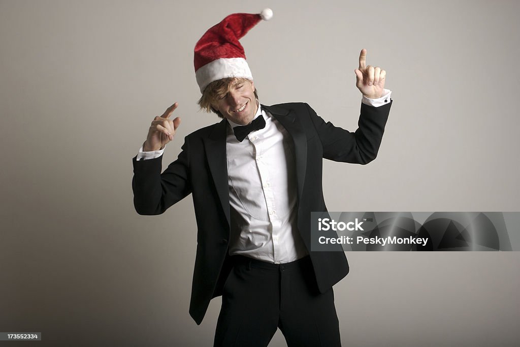 Man Celebrates Holidays Dancing in Santa Hat and Tuxedo Guy in a tuxedo and Santa hat rocks out with a smile Christmas Stock Photo