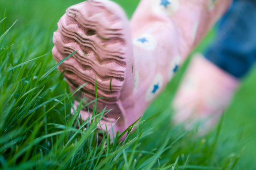 Close-up of pink wellie boots walking through green grass. Slight motion blur on toe of front of welly.