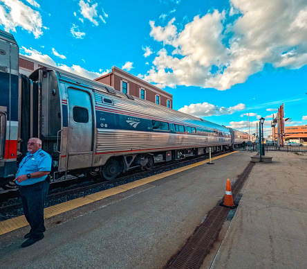 Springfield, Illinois, USA, October 7, 2023, Amtrak train stopped on the train tracks awaiting passengers to board. Train conductor stands next to the train to assist passengers boarding.