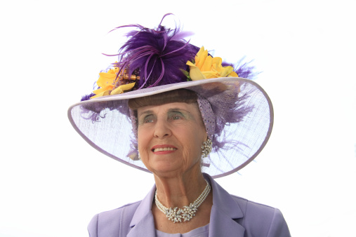 An old lady wearing a colourful hat with feathers and flowers