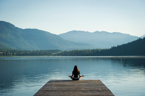 Woman doing sunrise yoga on Alta Lake in Whistler, Canada. Yoga and wellness themes.