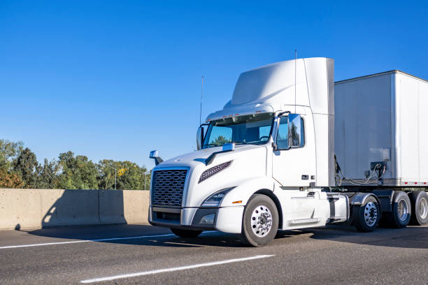 istock Powerful day cab white big rig semi truck with built-in roof spoiler transporting cargo in dry van semi trailer running on the road at sunny day 1735607222