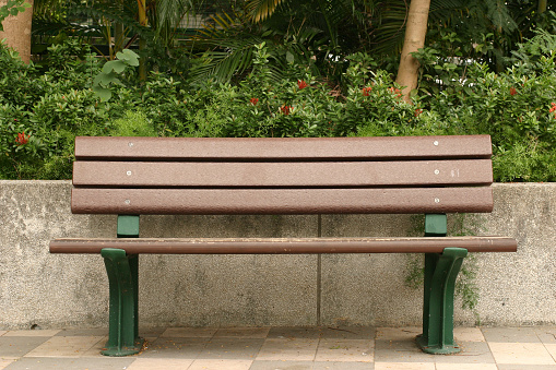wooden long bench, where the seating area is formed by rows of vertical planks and a backrest. notches are possible on the edges of the bench for inserting a bicycle tire. park with perennials