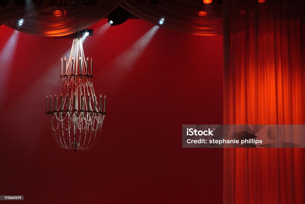 Stage Setting with Deep Red Curtains and Chandelier Image of an stage. A deep red curtain hangs on the right side and is illuminated with a spot light. A chandelier hangs on the left. Spot lights from above light up the fog in the air. Very dramatic composition. Image taken in low light conditions there is some noise. Curtain Stock Photo