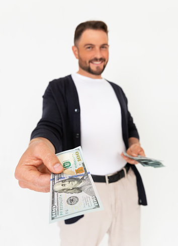 Young successful man holding out his hand with a 100 dollar bill on a white background. A man lends 100 dollars.