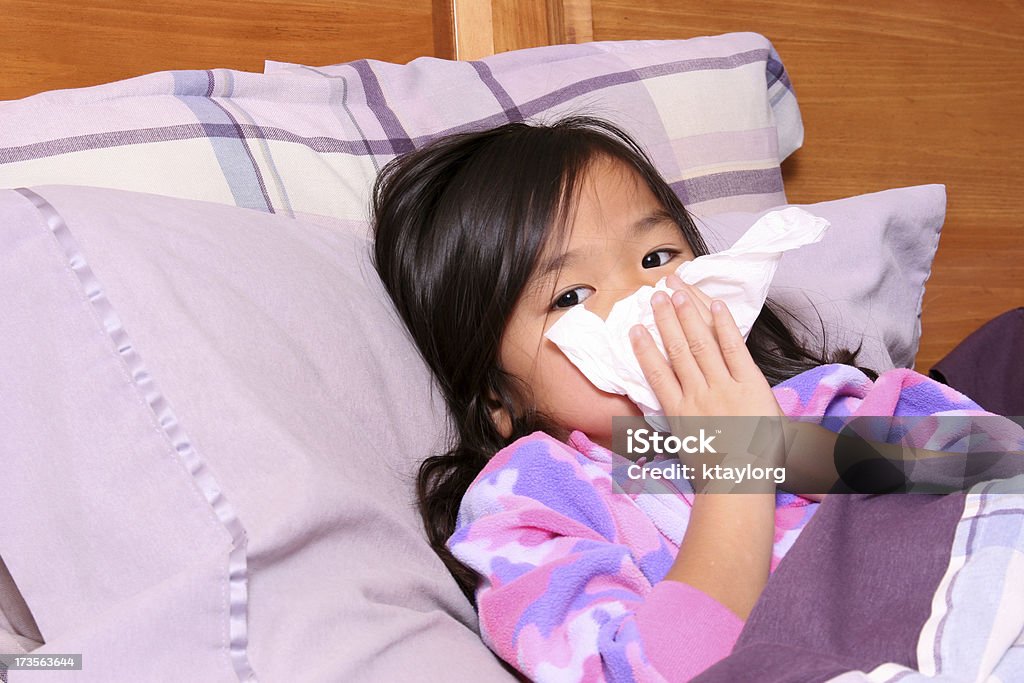 Chinese little girl blowing her nose Asian child lying in bed and holding tissue up to her runny nose Child Stock Photo