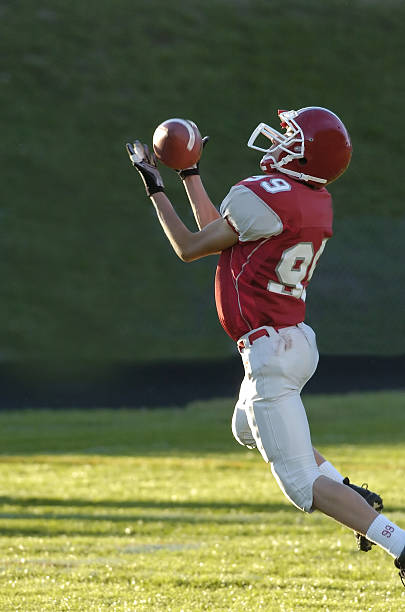 Football player jumping high above goal post – up into the clouds to catch touchdown pass.