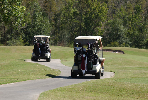 Golf carts driving away on a winding golf path during a charity tournament on a sunny day.  (all logos on bags and clubs removed or non-visible)