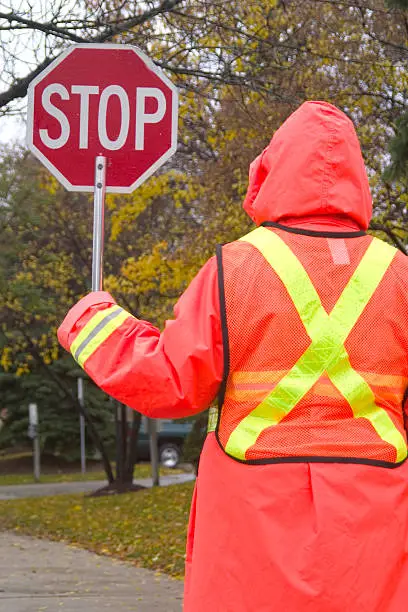 Crossing guard stops traffic on a rainy day. Wonderful contrast of colors. We have other crosswalk images in our portfolio.