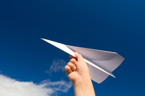 Boy's hand holding a paper aeroplane against a blue sky. Space for copy.