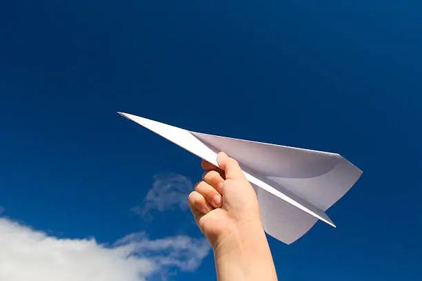 Photo of A hand holding a paper plane with the view of the sky