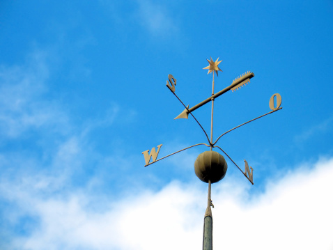 metal weather vane in the shape of a rooster to indicate the direction of the wind and the cardinal points on a background of the sky