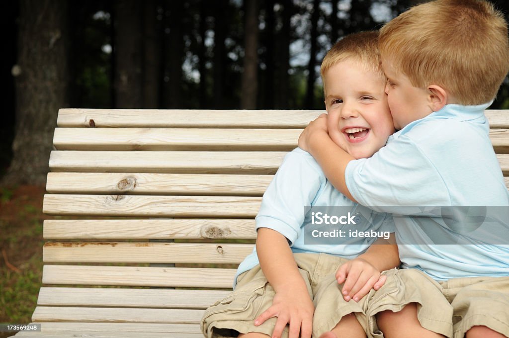 Twin Boys Laughing and Hugging on a Bench Outside Color photo of twin boys laughing and hugging on a bench outside. 2-3 Years Stock Photo