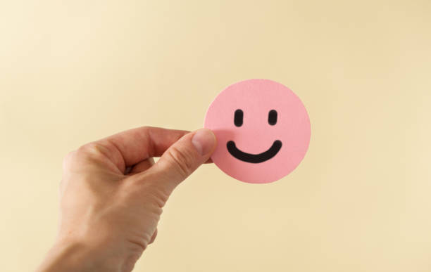 istock A hand holding pink happy face in beige background with copy space. Positive customer feedback and review. Happiness and Good service concept. 1735699575