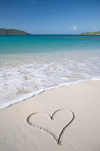 Single heart sits invitingly in the sand on the shore of a bright blue tropical sea
