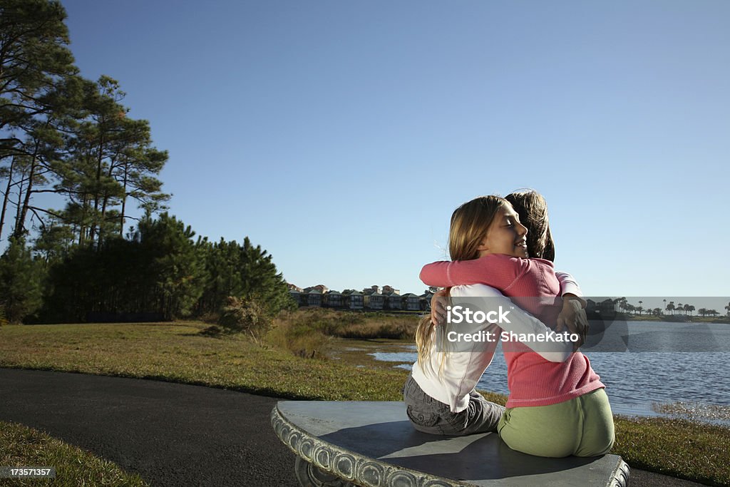 Najlepszymi przyjaciółmi objąć siedzi na ławce nad jeziorem Park - Zbiór zdjęć royalty-free (Dotykać)