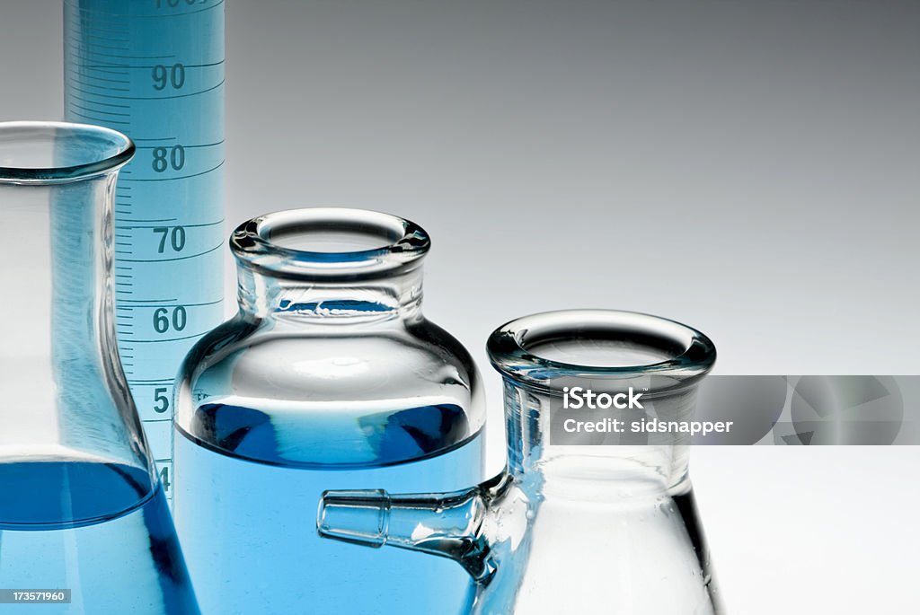 Glassware collection Tall measuring flask and other assorted laboratory glassware filled with blue liquid [ Back Lit Stock Photo