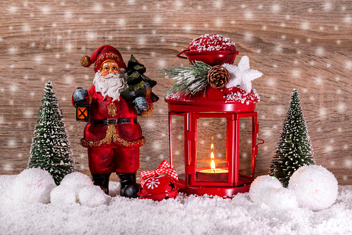 A Christmas lantern and a decorative Santa Claus in the snow are decorated with Christmas trees. Christmas and New Year decorations. Brown background.