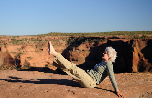 A woman in her 60s does Pilates at while relaxing at the rim of a desert canyon at sunset.