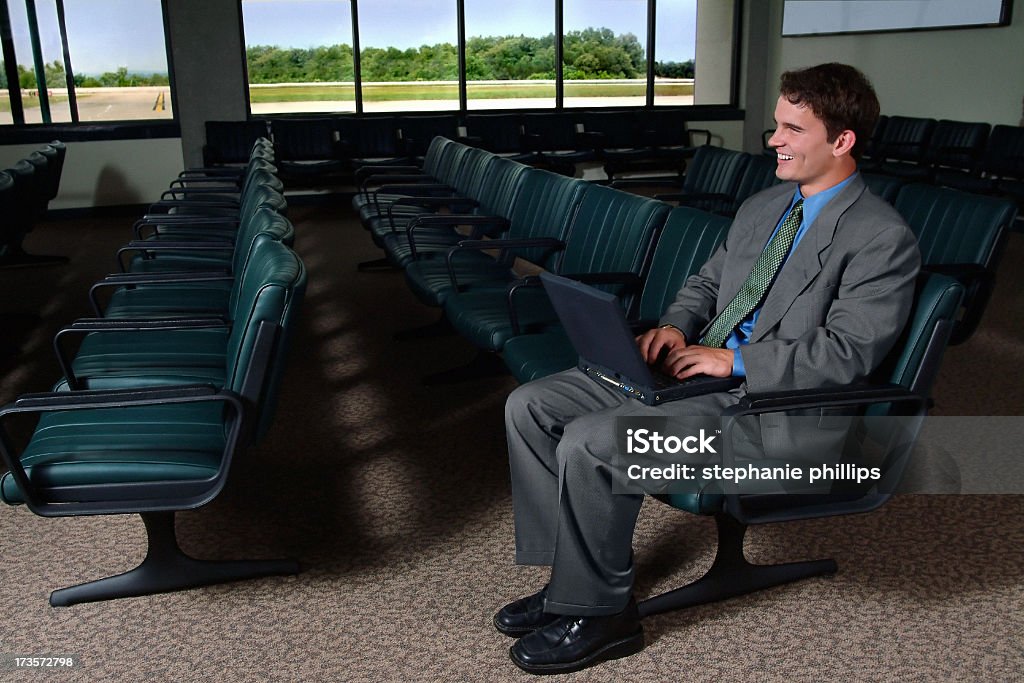 Young Man Working on his Laptop in an Airport Terminal Image of young businessman in airport terminal. He is happily using his laptop – probably surprised he is able to get wireless internet access. Businessman Stock Photo