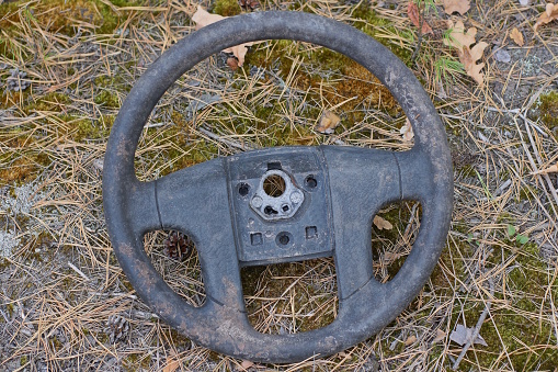 one old dirty round black car steering wheel lies on the ground and green moss on the street