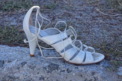 one white womens leather high heel sandal stands on the gray ground on the street