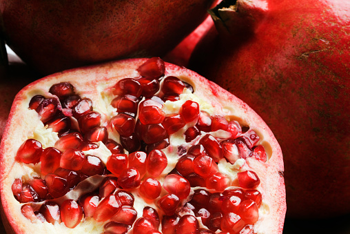 A pomegranate cut in half to reveal the fresh tropical fruit seeds inside. The halved fruit is shown in a close-up in the foreground, with additional whole fruits in the background. This luscious, wholesome food may be part of a diet for healthy eating.