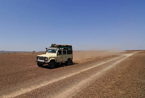 A safari fitted expedition Landrover driving through an African desert with a long dust trail behind it.