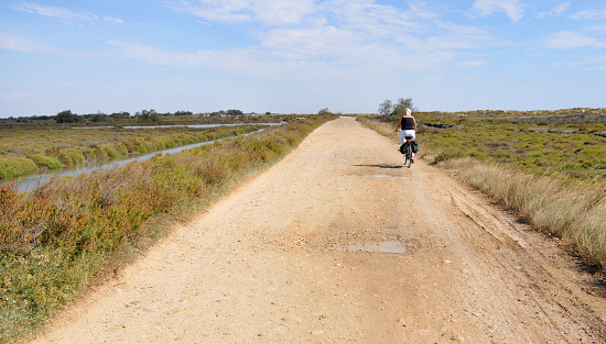 Senior woman cycling along a gravel road in the french Camargue. 