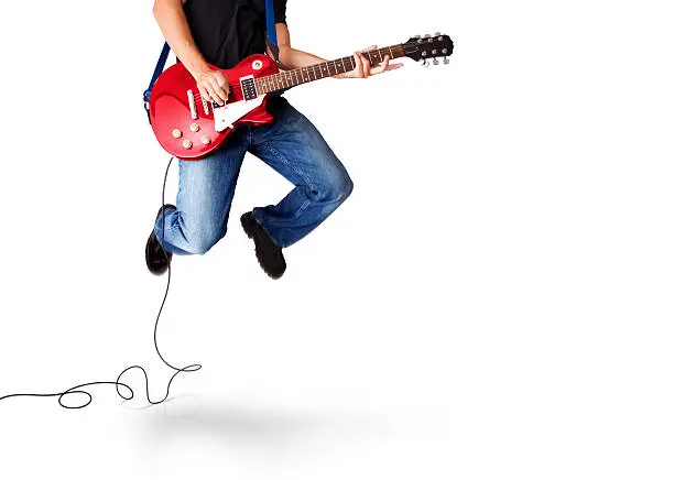 A man with a guitar jumps in the air while rockin' out.