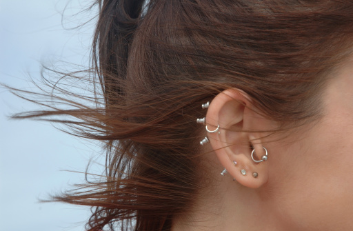 Close-up of multiple ear piercings on young woman with wind-swept hair. Slightly soft focus.