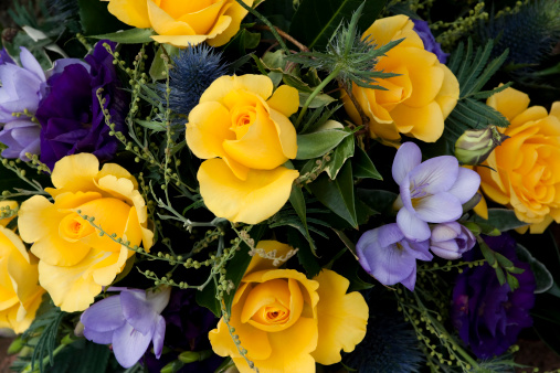Lilac coloured freesias with bright yellow roses and ornamental thistles in a bouquet.