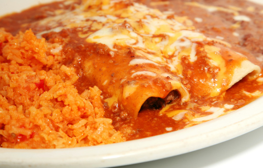 Yummy red beef enchiladas covered in melted cheese with refried beans and rice. Focal point are the enchilada.